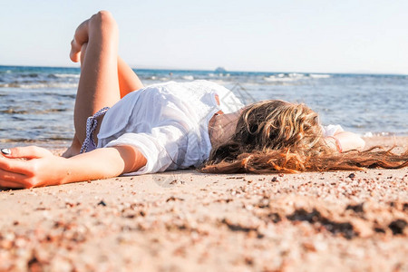 年轻的棕褐色金发女孩躺在靠近海边的沙图片