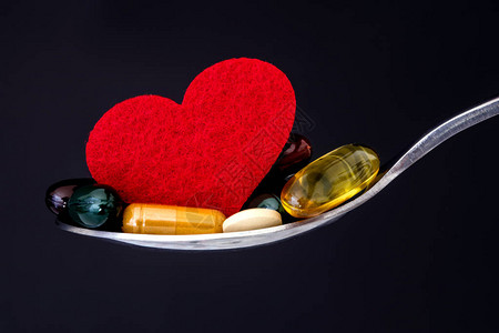 五颜六色的医疗补充剂和勺子里的红心药丸图片