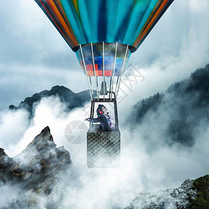 年轻女子一边听音乐一边享受她在热气球中的飞行乘坐热气球穿越山顶的云层图片