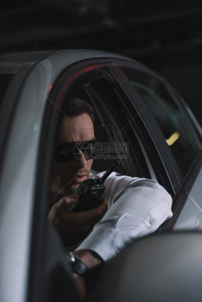 戴太阳眼镜的男便衣特工在汽车中监视和使用图片