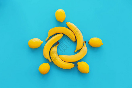 黄色香蕉在蓝纸时尚背景上与柠檬成圈图片