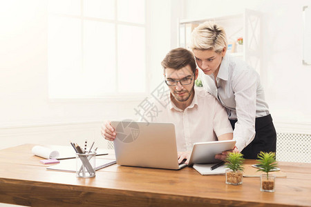 在现代办公室工作的几个严肃的年轻同事两名同事在笔记本电脑和数字平板电脑上工图片