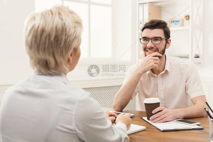 几个在现代办公室工作的年轻商业伙伴微笑的男人一边喝咖啡一边和同事讨论新项图片