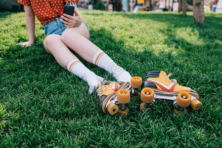 穿着袜子用智能手机在草地上靠溜冰鞋休息时使用智能手机图片