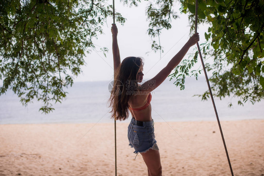 年轻女站在热带沙滩的绳子摆动上图片