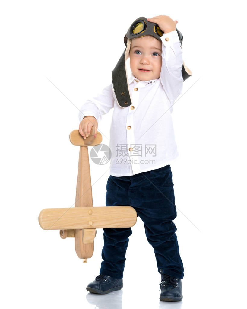 飞行员头盔中的男孩正在玩具木制飞机他梦想成为一名飞行员快乐童年的概念图片