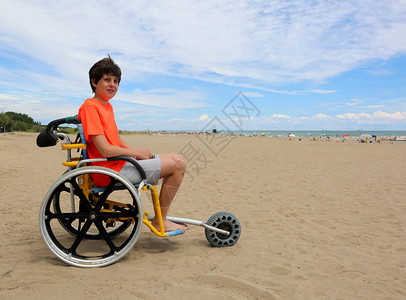 坐在特别轮椅上的小男孩用铝合金轮在海滩图片