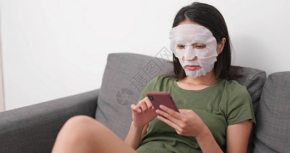 妇女脸部和手机上戴皮肤护皮纸面罩并图片