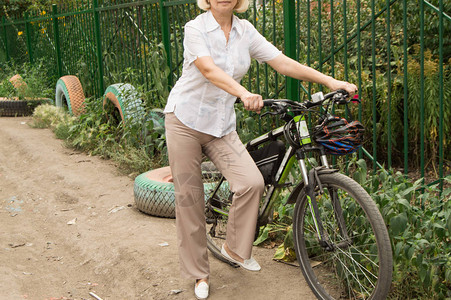 骑自行车的年轻快乐女人站在公园围栏图片