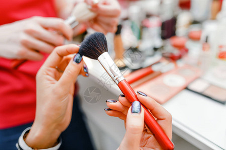 桌子背景上美容师女手中的专业化妆刷化妆品背景图片