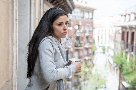 患有抑郁症的美丽的拉丁裔妇女在家里阳台上端着一杯咖啡图片