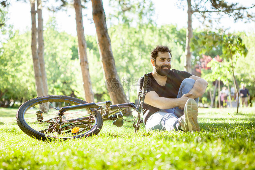 胡子男在公园旁边骑着自行车看离镜头远一点的照相机图片