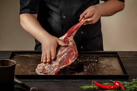 男厨师在木制餐桌上的石盘上用盐和胡椒来擦粗羊腿主厨为羊肉做开胃菜培训图片