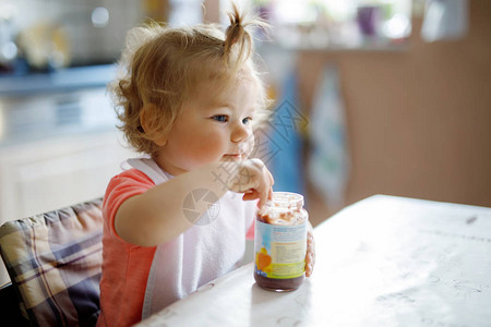 可爱的女婴吃勺子蔬菜或水果罐头食品儿童喂养和发展理念图片