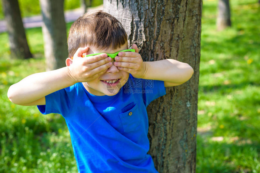 在森林背景的太阳镜上微笑着可爱的小男孩用手闭上两只眼睛图片