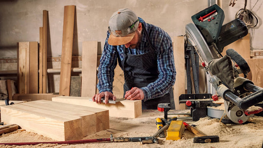 身着工作服的经验丰富的木匠和小企业主用尺子测量木板图片