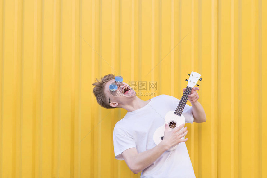 疯狂的年轻人在黄色背景上弹奏尤克里富有表现力的音乐家弹吉图片