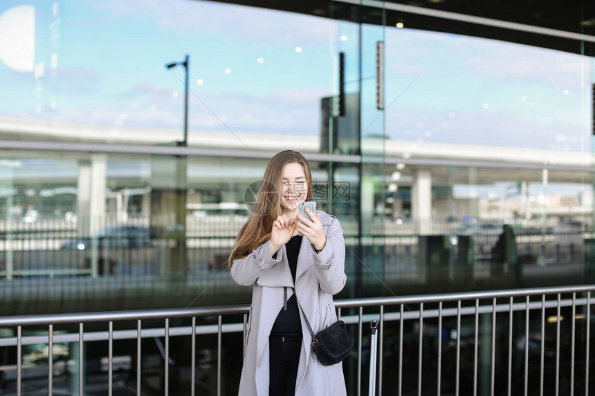 漂亮的商业女商人在Valise和机场附近用智能手机自拍图片