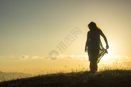穿着蓝色透明衣服的女孩日落时站在青草上在迷图片