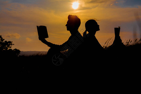 男人和女人在公园里看日落夫妇在天空日落时看书的剪影温暖的色调和柔的焦图片