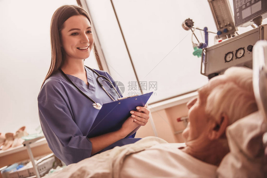 美丽的护士笑着和一位躺在医院病房床上的老人说话图片