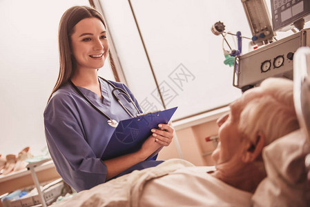 美丽的护士笑着和一位躺在医院病房床上的老人说话图片