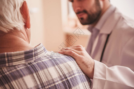 印有英俊医生与一名老人交谈手握在肩上和坐在医院病房里笑着微图片