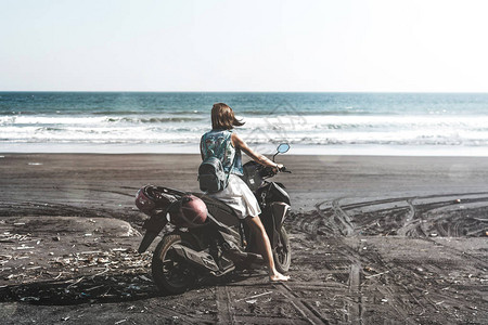 年轻女子驾驶摩托在海滩上用黑沙巴厘岛图片