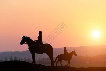 两个女孩骑着马在美丽的日落背景下图片
