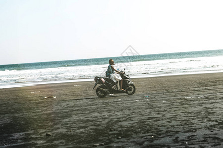 年轻女子驾驶摩托在海滩上用黑沙巴厘岛图片
