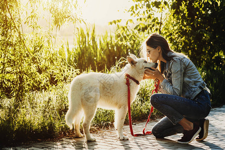 美丽的caucasian年轻女子早上在公园散步时亲吻白极狗图片