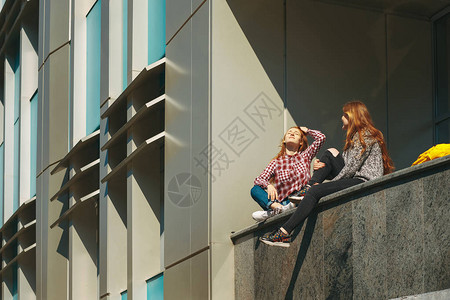 大学生课后休息一头红发的年轻女孩坐在校园户外窗户附近的一栋现代建筑上图片
