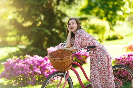 穿着长的粉红色花裙的时髦年轻女子的肖像停下来骑着老式自行车图片