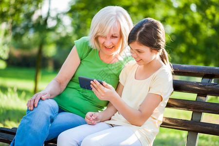 祖母和孙女坐在公园里使用手机图片