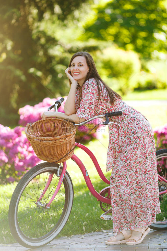 穿着长的粉红色花裙的时髦年轻女子的肖像停下来骑着老式自行车图片