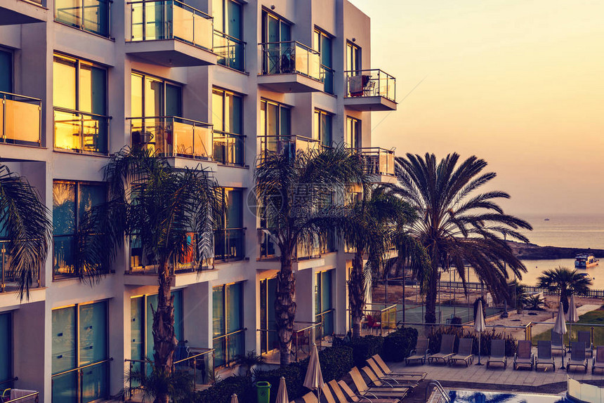 查看反映温暖日出的酒店窗户酒店游泳池棕榈树小船和大海的背景负拷贝空间图片
