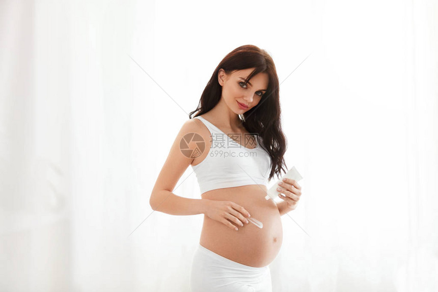 怀孕的皮肤护理美丽的孕妇在家中施用贝利腹图片