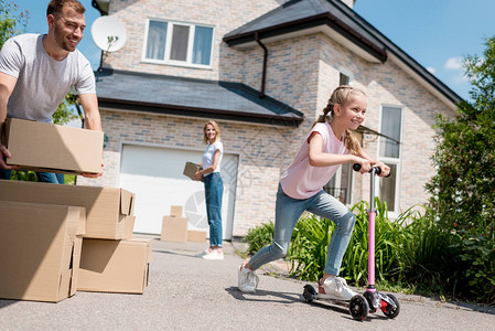 小孩子骑着滑板车和她的父母拆开纸板箱搬进新房子图片