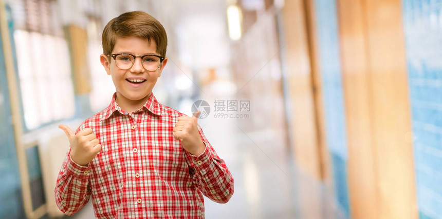 带着绿眼睛笑着微笑的青眼健壮的幼童向照相机举起手势表示喜欢和在学校图片