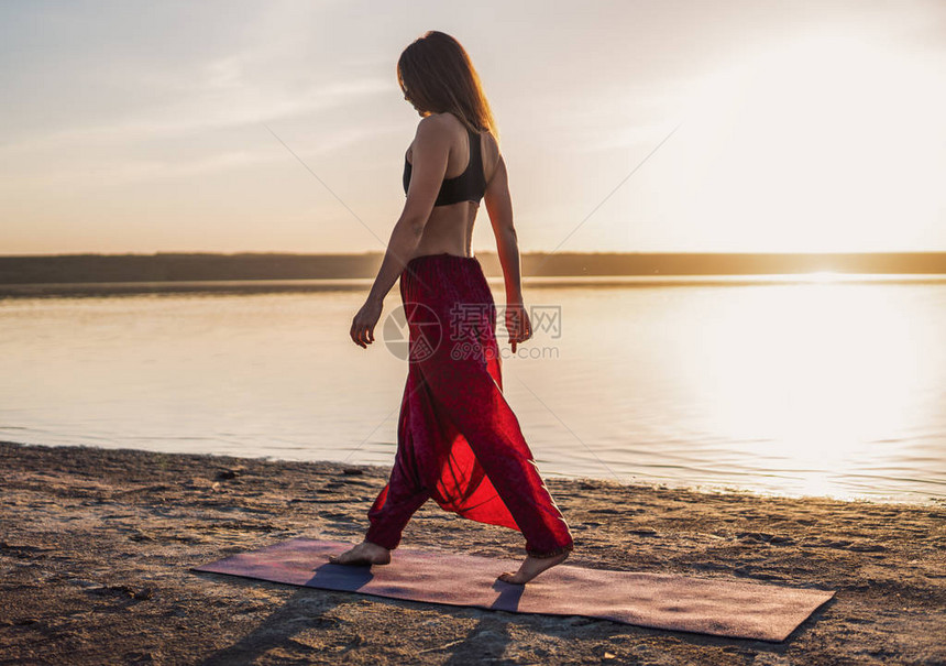 日落时在沙滩上的妇女开始瑜伽训练图片