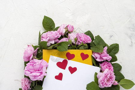 粉红色的玫瑰围绕着一本黄色的书白色的床单和浅色石头背景上的红心图片
