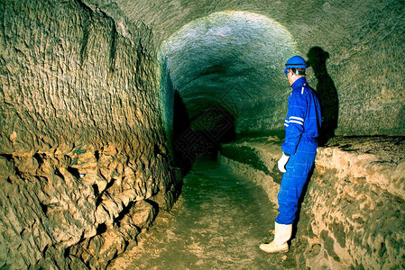 地下工作身着蓝色整体和安全头盔的驼背工人站在地下隧道中工作人员检查地图片