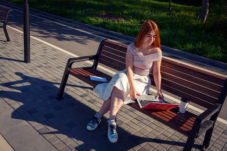一位身穿白色浪漫裙子粉色上衣和蓝色运动鞋的红发年轻女子喝咖啡图片