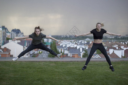 两个年轻的女体操运动员做杂技运动跳跃与城市风景图片
