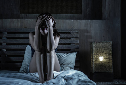 年轻的悲伤和抑郁的女人坐在床上图片