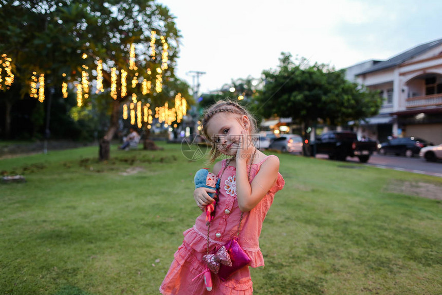 穿粉红色裙子的小女孩和玩具站在城市草坪上图片