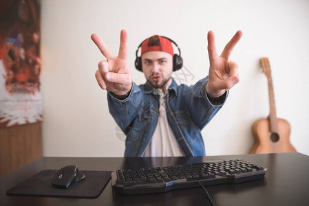 快乐的人是一个在手中表现出和平标志的游戏玩家玩电脑游戏时戴着耳机图片