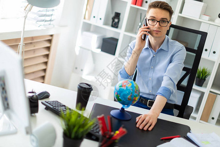 一个戴着眼镜蓝色裤子和一件浅色衬衫的英俊年轻人正在办公室工作椅背上挂着他的夹克背景图片