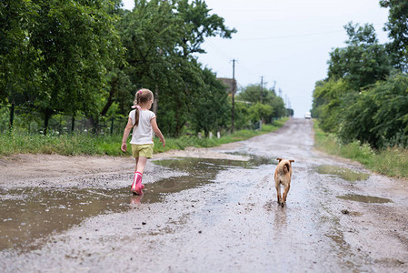 四岁的可爱女孩在雨后湿断的路上行走图片
