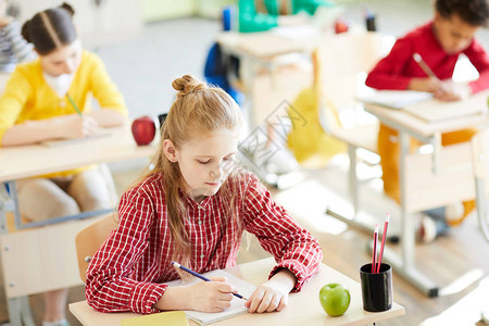 勤奋的女学生在同学们中倾斜于她的书本图片